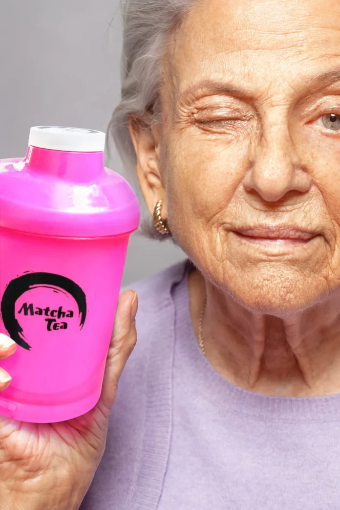 Seniorka se stříbrnými vlasy drží růžový šejkr s logem Matcha Tea