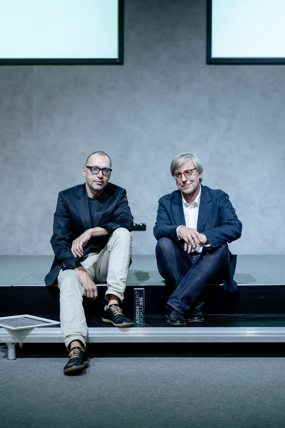 Architekt roku 2026 získali Ehl a Koumar, Architekt obci Libčice 1 Architekti Lukáš Ehl a Tomáš Koumar sedí na hraně pódia, mezi nimi leží skleněná cena Architekt roku 2026