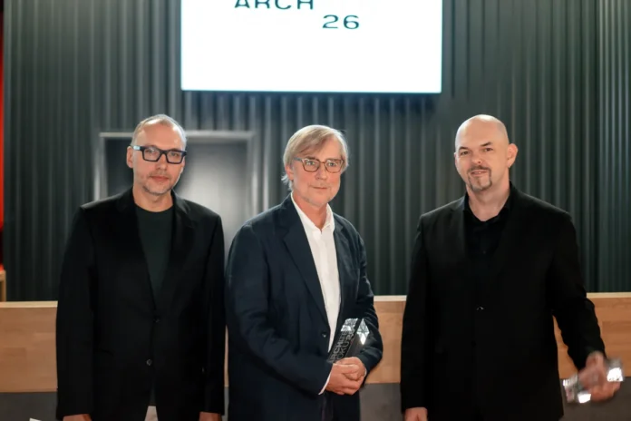Lukáš Ehl, Tomáš Koumar se skleněnou cenou Architekt roku 2026 a Milan Kopeček stojí před plátnem s logem soutěže