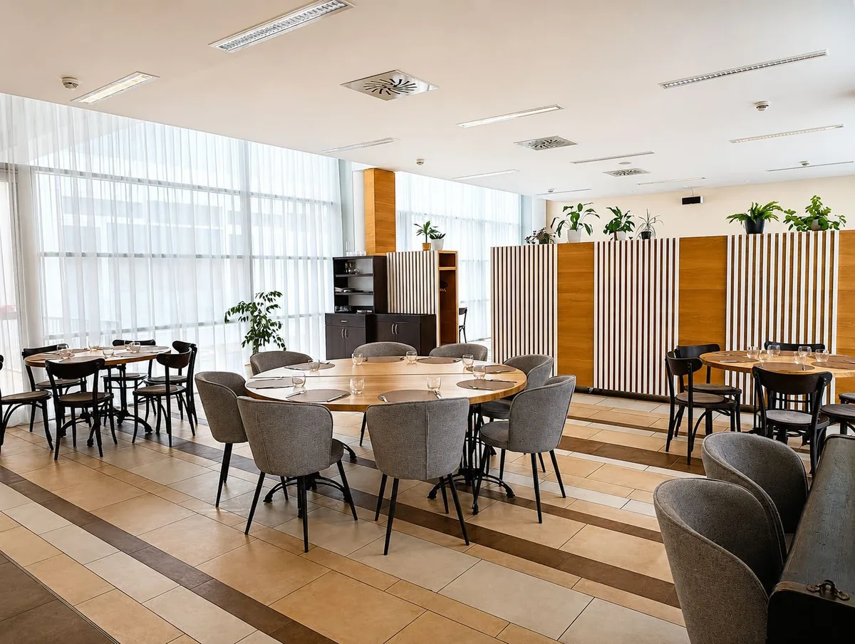 Earnest v Kroměříži: kavárna, restaurace a bowling v Domě kultury 2 Sál restaurace Earnest s prostřeným kulatým stolem, šedými čalouněnými židlemi a dřevěnými lamelami na stěně
