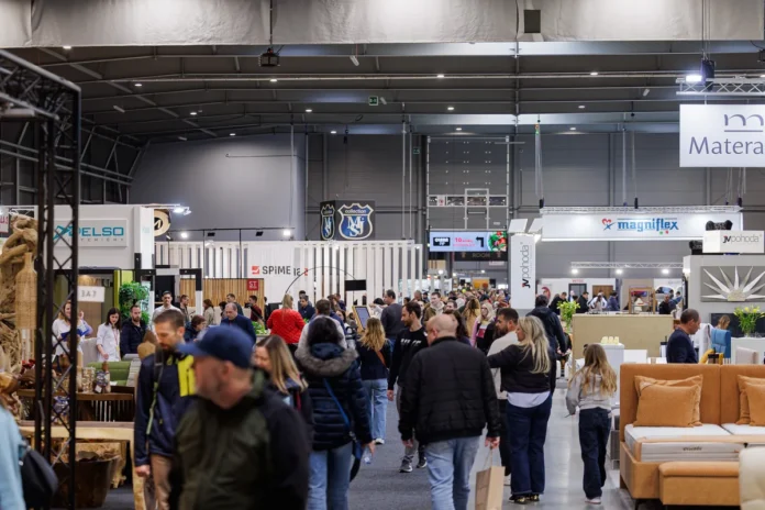 Zaplněná hala veletrhu FOR INTERIOR v PVA EXPO PRAHA, návštěvníci procházejí uličkou mezi stánky Magniflex, JV Pohoda a Delso Interiéry, vpravo béžová čalouněná pohovka