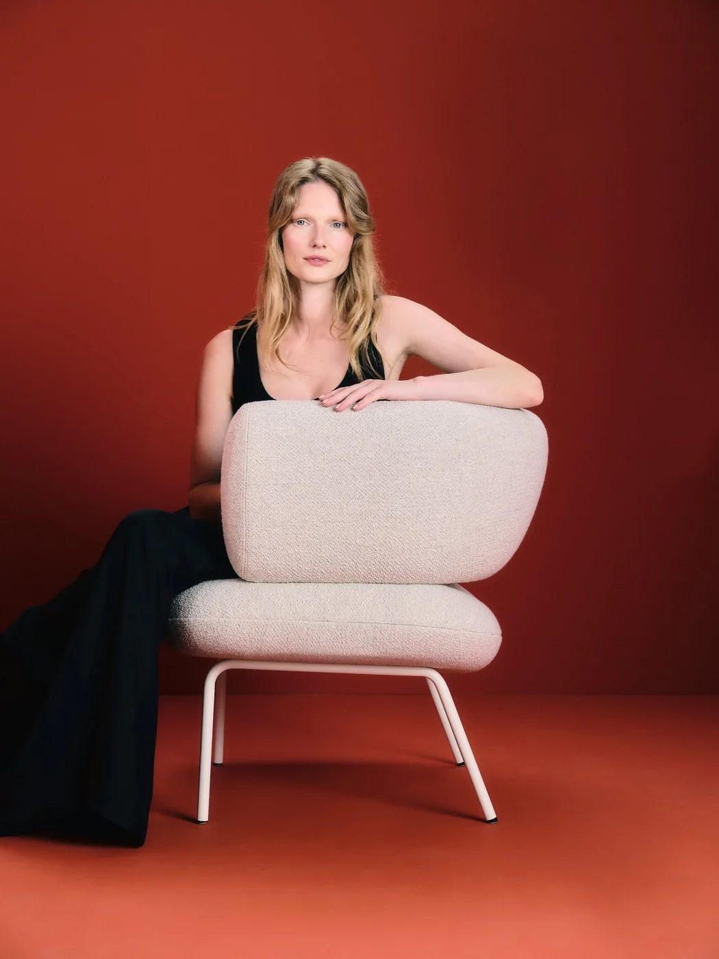 Z jednoho křesla celá kolekce: Lucie Koldová navrhla pro LD Seating sezení Dafna 2 Žena opřená o bílou čalouněnou židli Dafna s ocelovou podnoží na červeném pozadí
