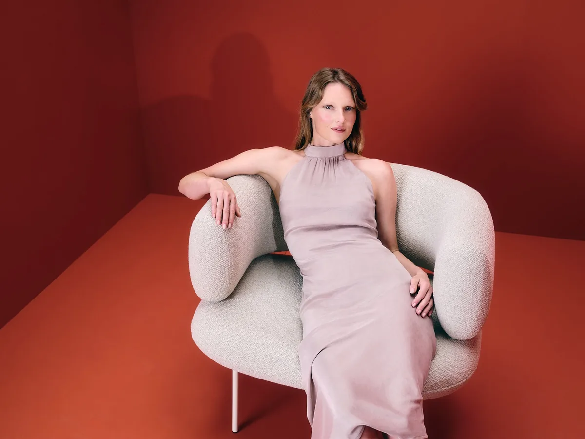 Z jednoho křesla celá kolekce: Lucie Koldová navrhla pro LD Seating sezení Dafna 3 Žena v růžových šatech sedí v bílém křesle Dafna na červeném pozadí